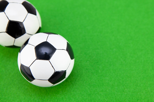 Two miniature black and white footballs on a green felt surface with copy space to the right