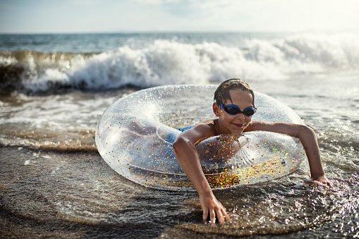 Little boy having fun in the sea. The boy is floating in inflatable ring and the waves are crashing on him. Sunny summer day.\nNikon D850