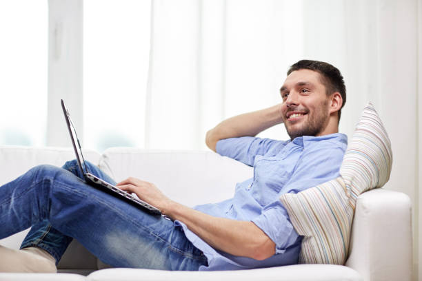 istock smiling man lying on couch with laptop at home 1268415957