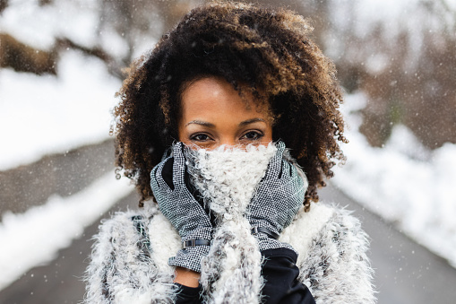 Woman covering her mouth with wool warm scarf under the snow in cold winter.