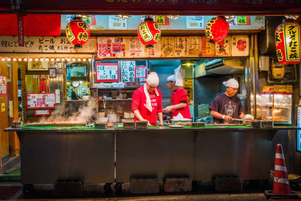 Osaka chefs cooking traditional food street stall night Amerikamura Japan Three chefs cooking traditional street food at a pavement stall at night in the popular Amerikamura district of central Osaka, Japan’s vibrant second city. takoyaki photos stock pictures, royalty-free photos & images