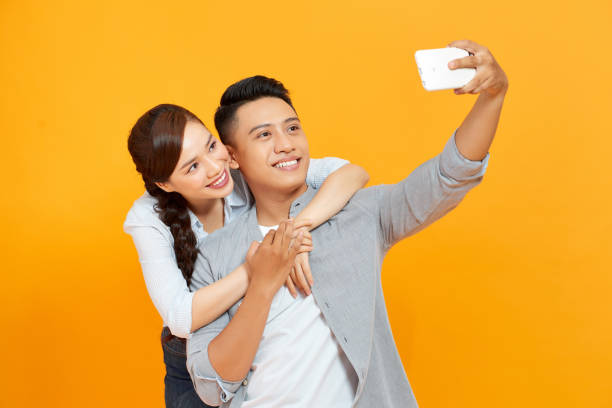 istock Young and beautiful couple expressing joy on camera while partying and taking selfie isolated over yellow background. 1268429250