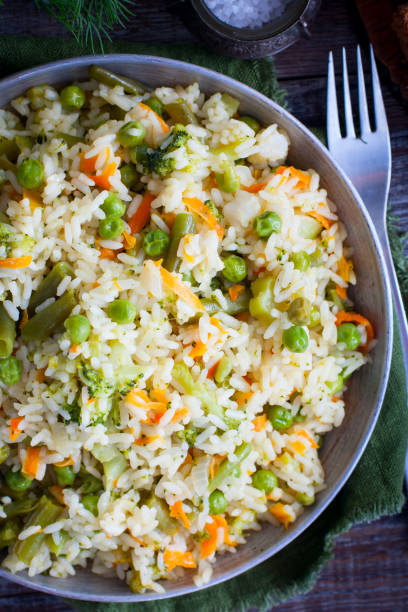 Rice with vegetables - carrots, onions, broccoli, pepper, green peas in a frying pan on a wooden table, selective focus