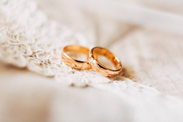 zwei goldene eheringe für die braut und bräutigam mit einem edelstein auf weißer spitze. - jewelry gem gold reflection stock-fotos und bilder