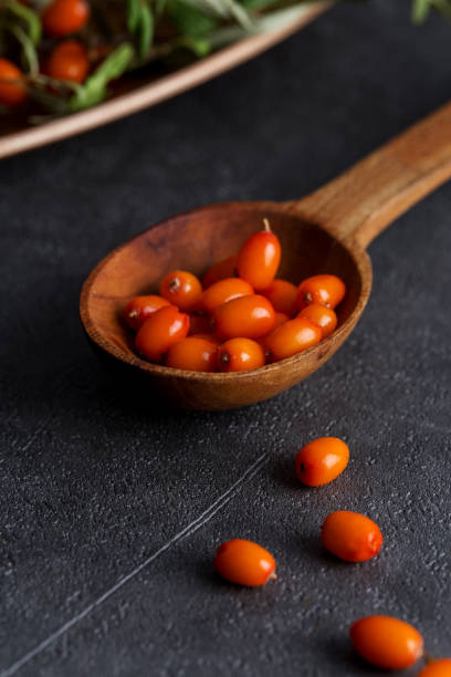 Close up wooden spoon with berries of sea-buckthorn at dark textured background Close up wooden spoon with berries of sea-buckthorn at dark textured background. Concept of medical herb and berries. autumn copy space rural scene curing stock pictures, royalty-free photos & images