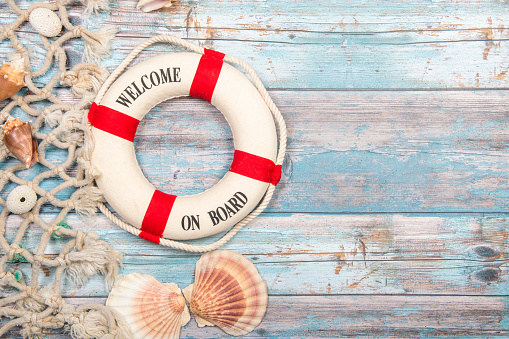 Nautica background with safety buoy with the text welcome on board seashells and fishing net on a blue scaffolding wooden background