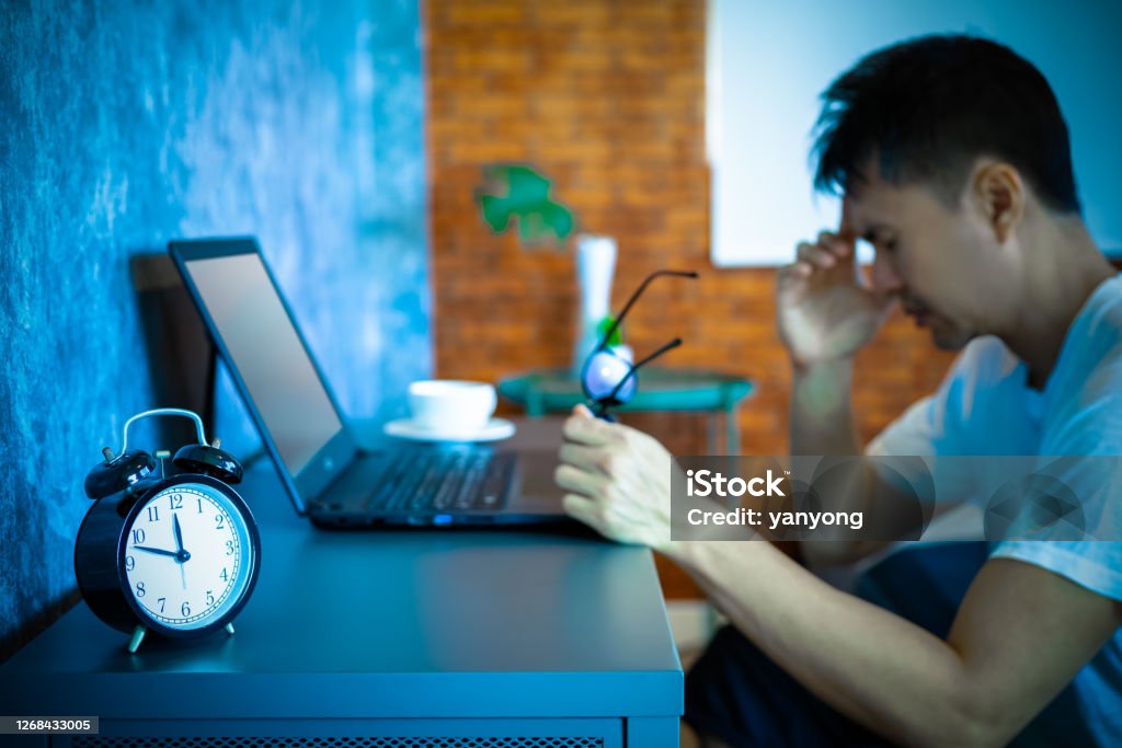 headache, tense young asian man working on laptop computer in bedroom at night Staring Stock Photo