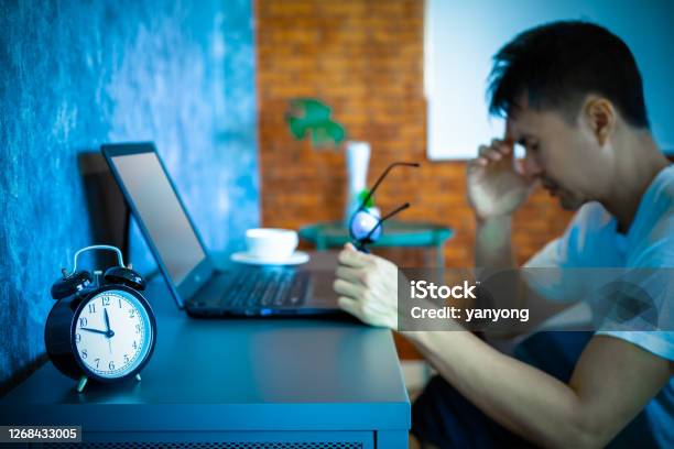 Headache Tense Young Asian Man Working On Laptop Computer In Bedroom At Night Stock Photo - Download Image Now