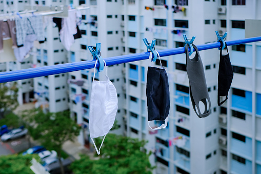 Reusable masks washed and hung on laundry pole to dry;  eco-friendly, reusable homemade cloth masks, biocompatible supermask PM2.5. Sustainable and environmentally-friendly. HDB flats in background