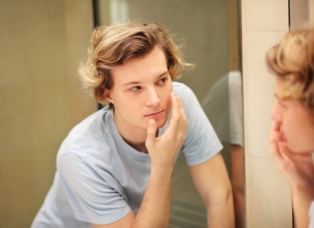 istock young man looking in the mirror,combing his hair,looking at problems on face 1268436980