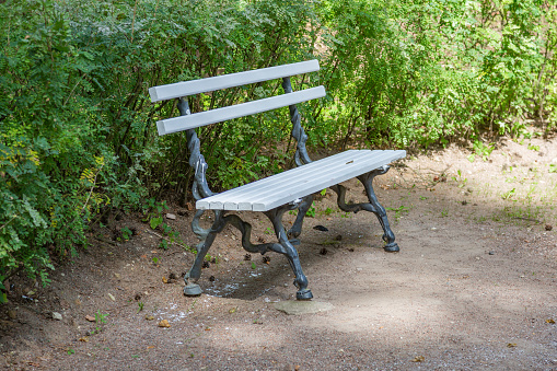 A recreation bench made of white boards and wrought iron in a city park in summer
