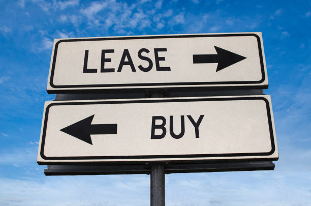 Lease vs buy. White two street signs with arrow on metal pole with word. Directional road. Crossroads Road Sign, Two Arrow. Blue sky background. Concept for own property versus borrow it. stock photo