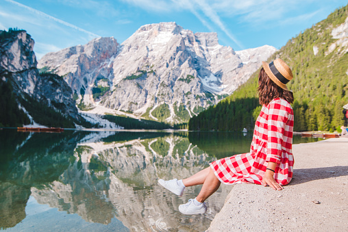 woman in red checkered dress with straw hat looking at mountain lake. summer vacation. travel concept