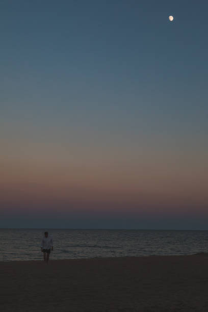 istock man standing at sea beach looking at moon 1268440441