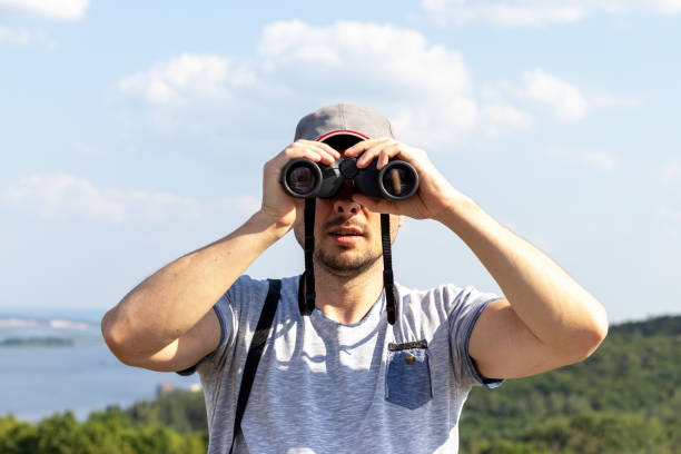 istock A man looking at camera through binoculars against a scenic view of a wide river on a hill on a sunny day 1268441846