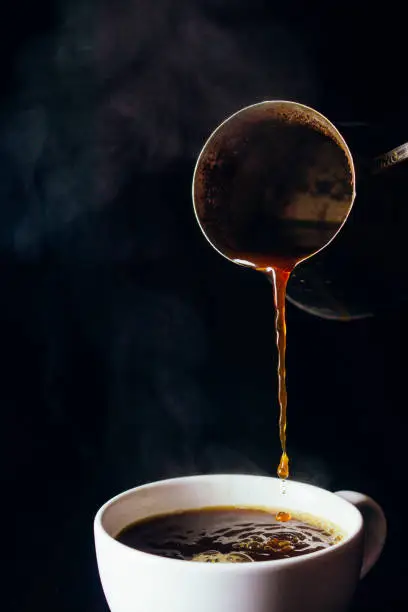 Photo of Hot coffee is poured from the turk into a white Cup