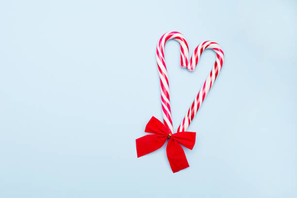 istock Two Candy Canes in Heart Shape with Red Bow on blue Background. copy space 1268453246