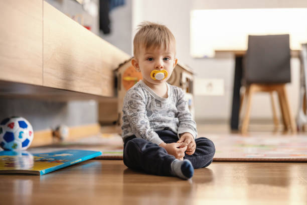 istock Cute little boy sitting at home with pacifier in his mouth. 1268463397