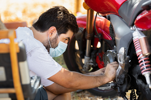 Young man with protective mask repairs his motorbike at home in the garden