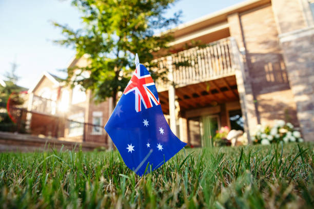 australian flag standing on green grass in front of a house. australia day national holiday celebration. real estate property for buy and sell in australia market. - australia australia day celebration flag imagens e fotografias de stock