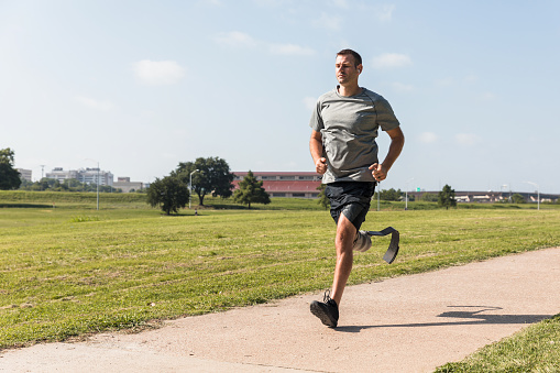 In the morning, the mid adult military veteran uses his specialized prosthesis to run on the track in the park.