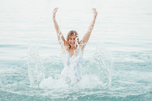 Young woman splashes full of happiness with the water in the sea