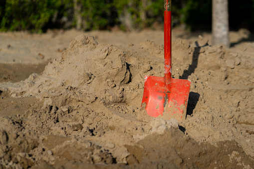 A red shovel (working equipment of construction industrial) is stabbing on the sand bulk.