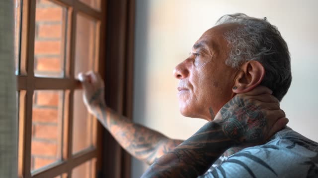Worried mature man looking through window contemplating and thinking at home