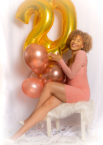 Young beautiful African American light skin green eyed woman celebrating her 20th birthday with balloons and confetti photo shoot