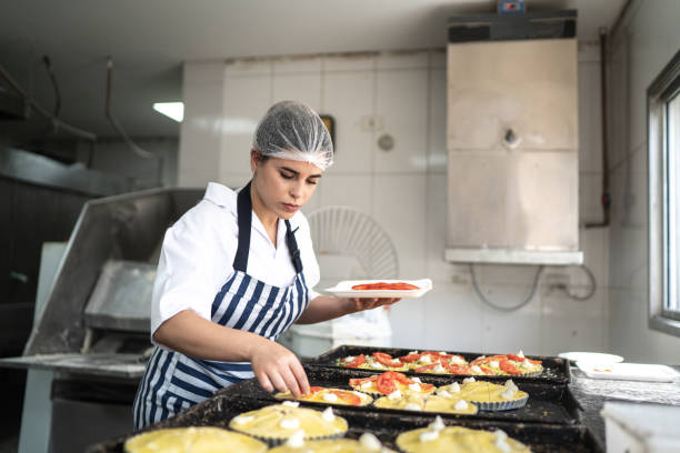 bäckerfrau bereitet mini-pizzen in der kommerziellen küche - hair net stock-fotos und bilder