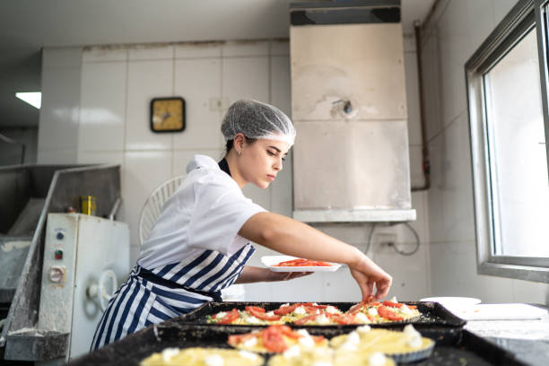 bäckerfrau bereitet mini-pizzen in der kommerziellen küche - hair net stock-fotos und bilder