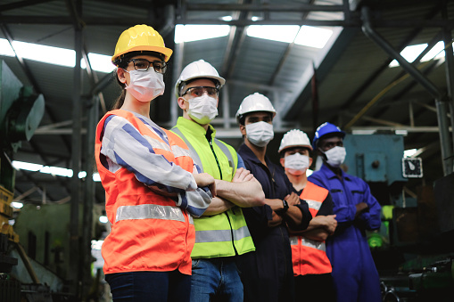Industrial woman engineer wearing  hygiene face mask and hardhat with workers in factory,new normal of industry for protection covid-19 pandemic.