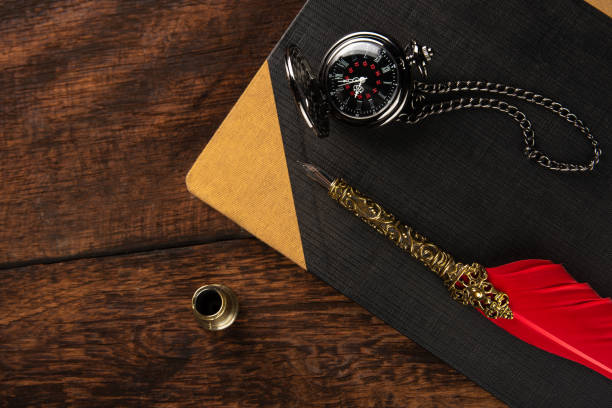istock Fountain pen with red feather on a notebook and an old watch, Top view. 1268490060