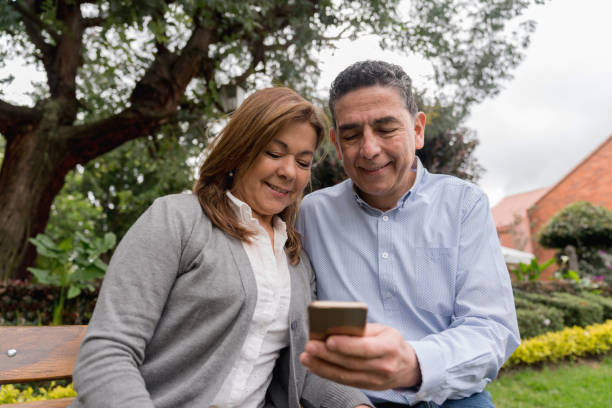 couple sitting at the park looking at social media on a cell phone - using phone garden bench imagens e fotografias de stock