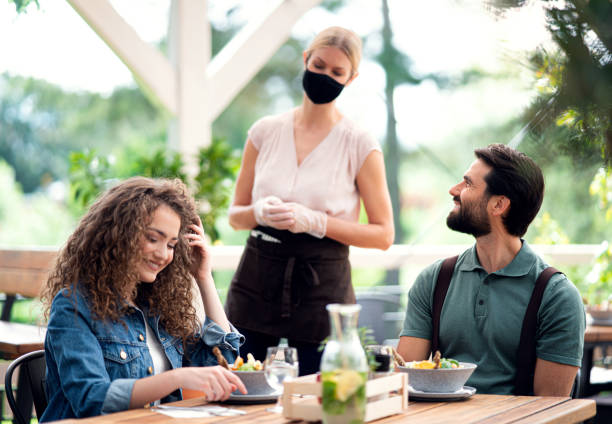 istock Waitress with face mask serving happy couple outdoors on terrace restaurant. 1268490649
