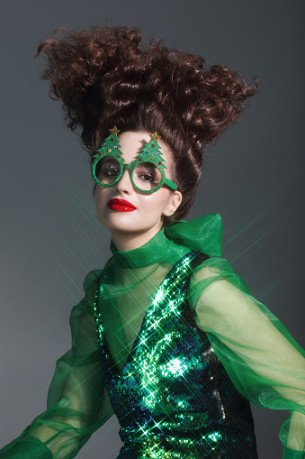 Fashionable young woman wearing funny Christmas party glasses and green sequin dress