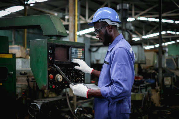 afroamerikanische fabrikarbeiter in der verwendung von laptop und drucktasten, um die maschine zu testen. - manual worker portrait helmet technology stock-fotos und bilder