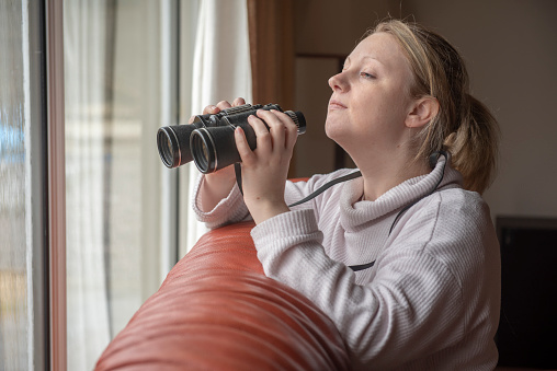 Women in late twenties spying with binoculars through a window