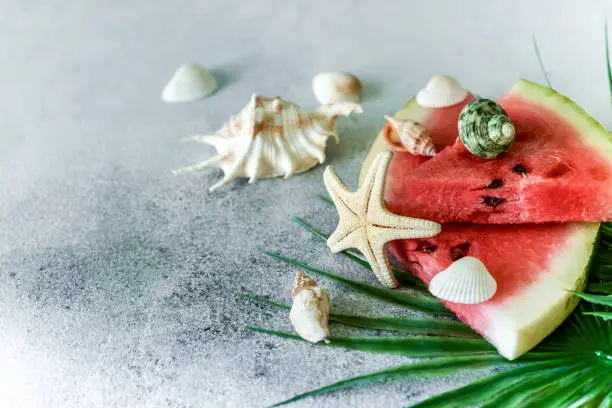 Photo of A healthy diet berry with seashells, stars and palm leaves. Sweet tasty popsicles a slice of watermelon in summer on a light background. copy space for designer