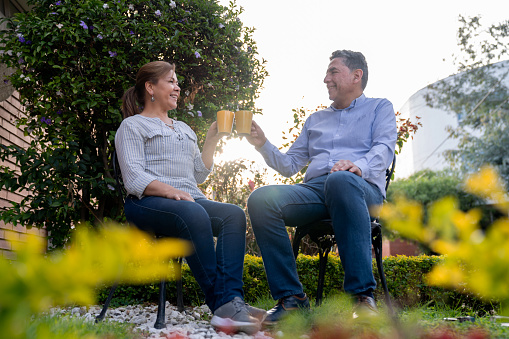 Happy adult Latin American couple drinking a cup of coffee in the garden and smiling - lifestyle concepts