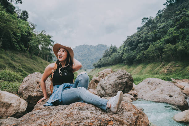 istock Happy woman laughing while sitting on the rock by river in mountain 1268497235