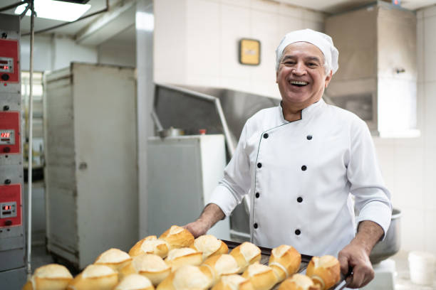 ritratto di un fornaio anziano che tiene in mano un vassoio pieno di pane - baking baker bakery bread foto e immagini stock