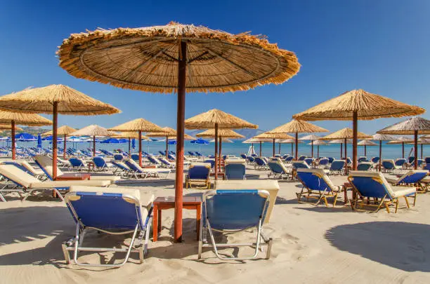 Straw beach umbrellas and sun chairs on a sandy beach on the east coast of Zakynthos island in Greece