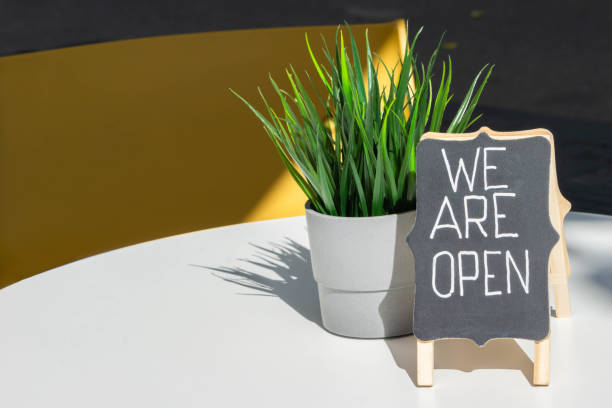 istock Handwritten WE ARE OPEN sign and grass pot closeup on open-air cafe table 1268504268