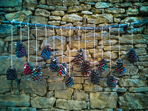 Homemade painted pinecones hanging from a string on a stone wall as decoration of a facade