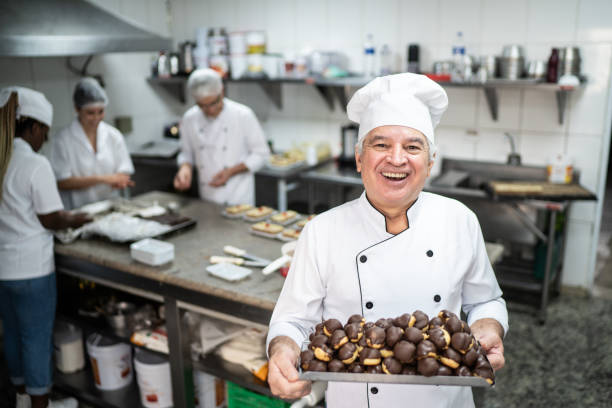 Happy senior chef carrying a tray full of eclairs Happy senior chef carrying a tray full of eclairs old candy store stock pictures, royalty-free photos & images