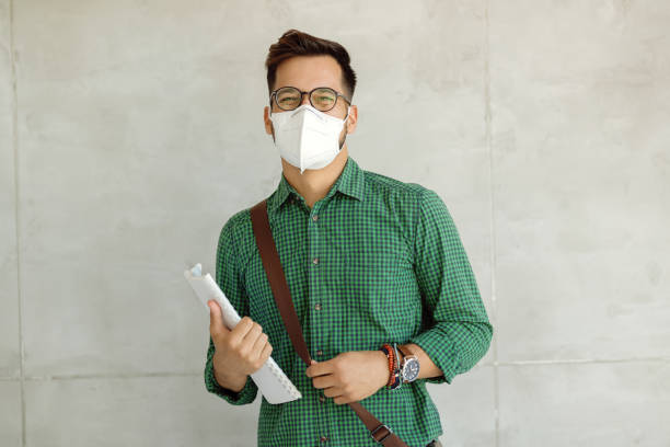 Happy college student with protective face mask against the wall.