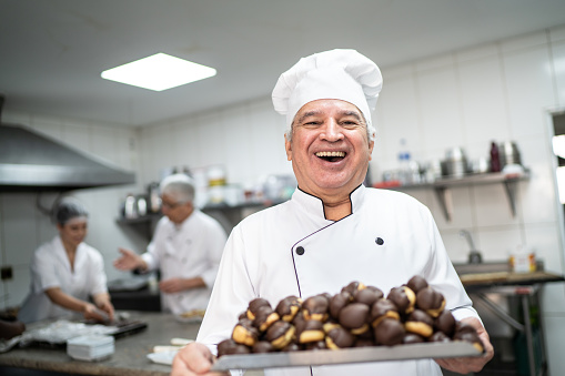 Happy senior chef carrying a tray full of eclairs