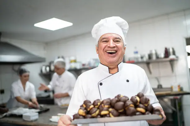 Photo of Happy senior chef carrying a tray full of eclairs