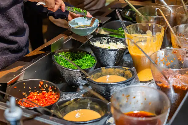 Customize hotpot colorful sauce at the station in restaurant, a wide variety of choices available. Hand is mixing sauces.